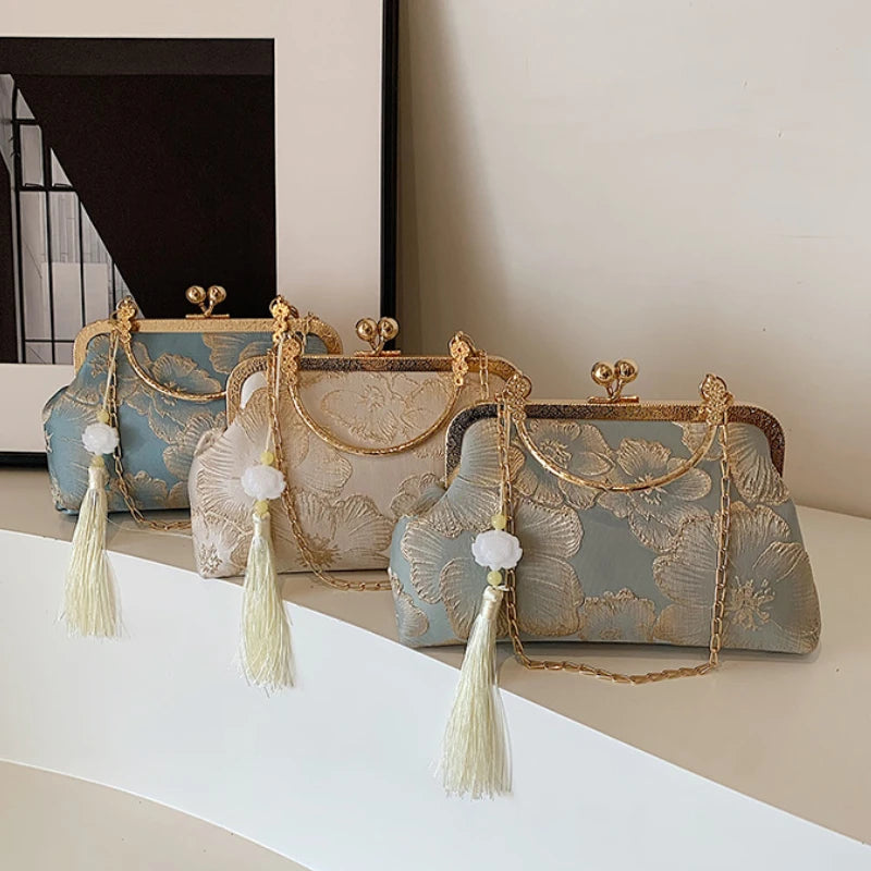 A collection of embroidered silk evening clutches in blue and beige tones with gold chain straps displayed on a white surface