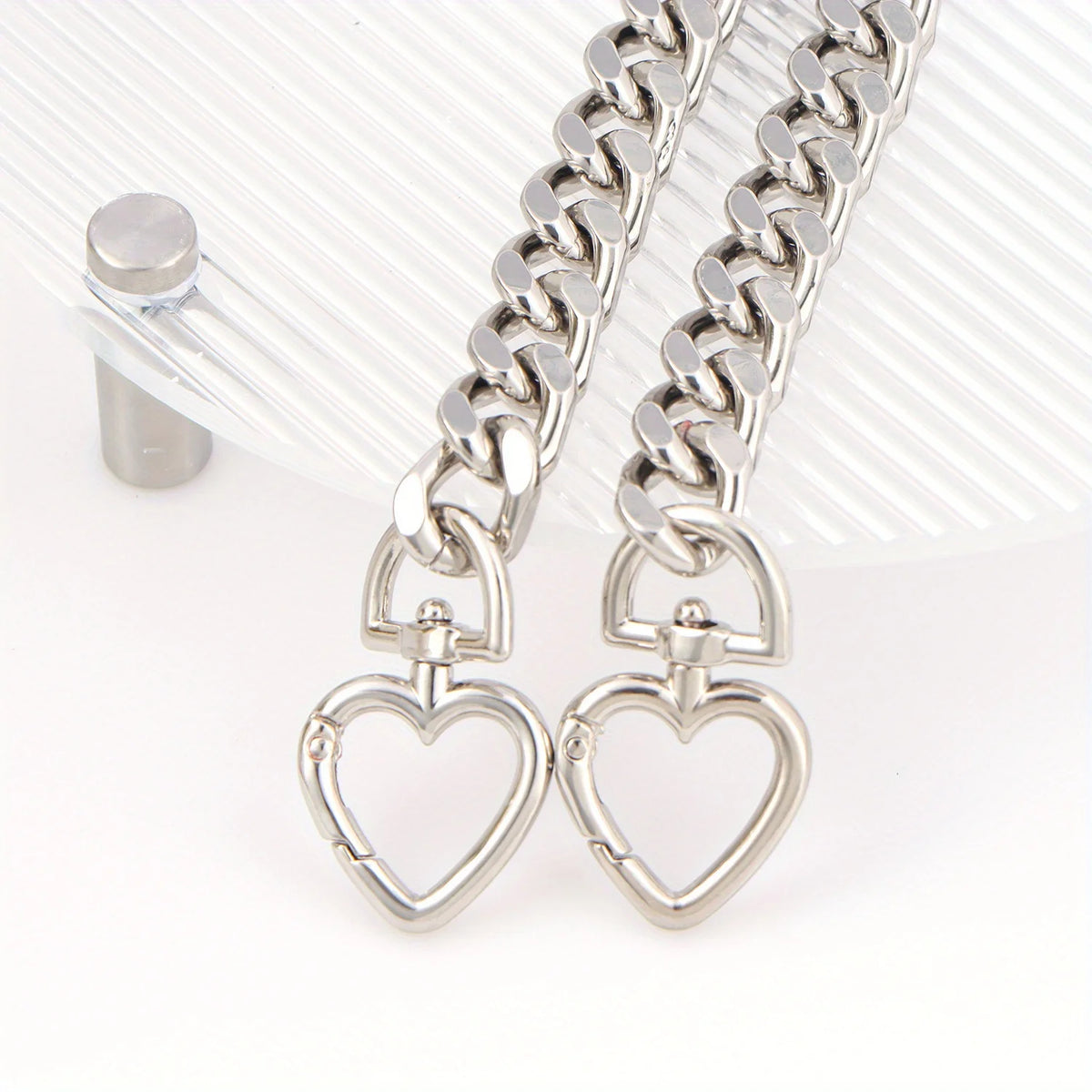 Silver heart-shaped metal purse chain extender with a link chain displayed on a clear acrylic surface.