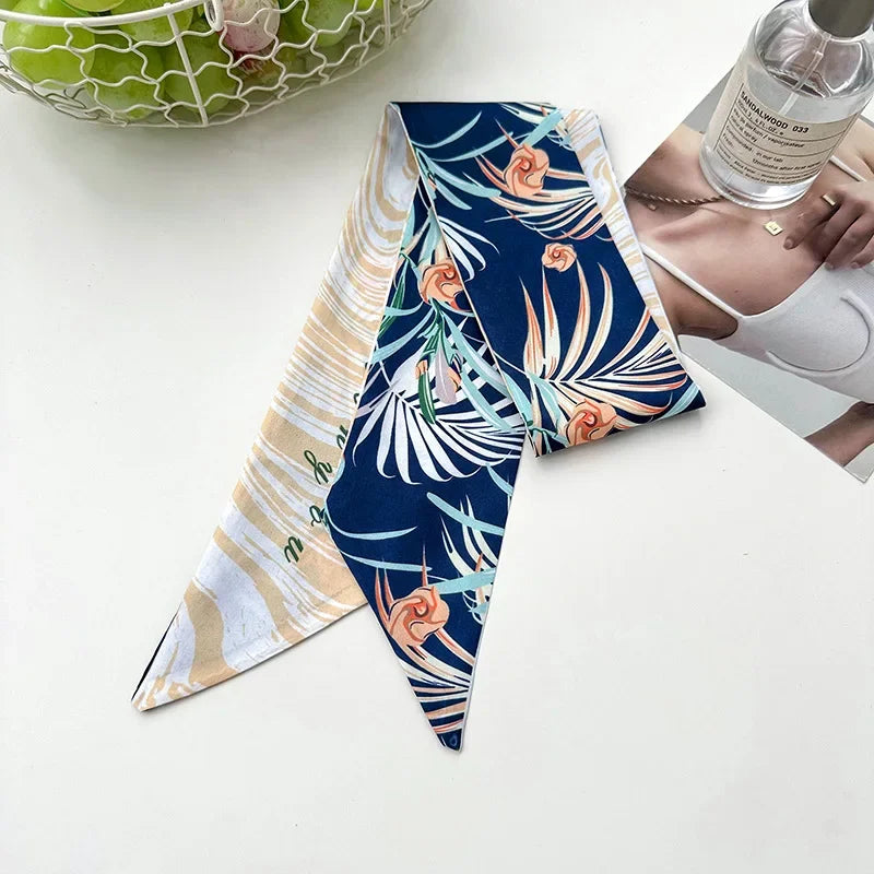 Foulard floral en soie plié, motif bleu marine et orange sur fond blanc.
