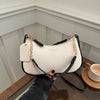 A cream and black crescent crossbody bag with gold hardware is held by a hand on a wooden surface.