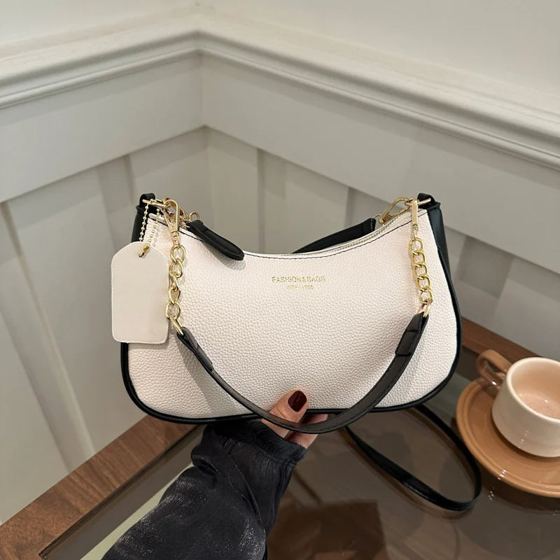 A cream and black crescent crossbody bag with gold hardware is held by a hand on a wooden surface.