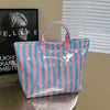 A pink and blue striped waterproof PVC tote bag with a pink handle resting on a wooden surface.