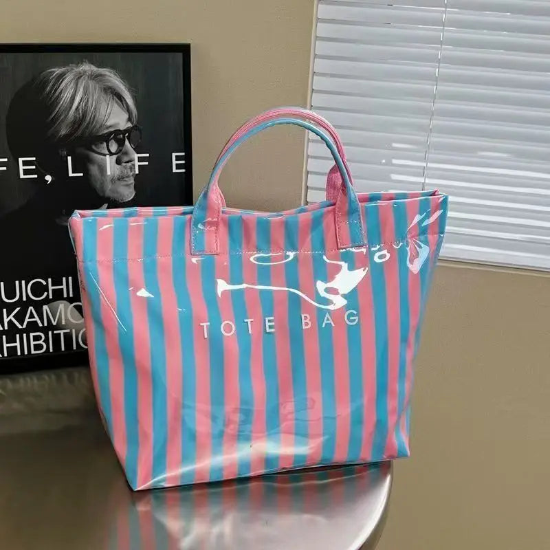 A pink and blue striped waterproof PVC tote bag with a pink handle resting on a wooden surface.