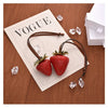 Charmoche en cuir marron avec un charme de fraise rouge sur du papier portant le mot VOGUE.