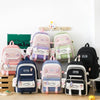 A set of five pink and green nylon backpacks with cartoon designs displayed on a wooden surface.