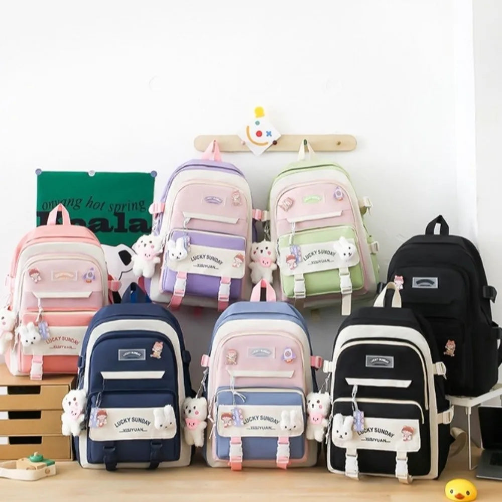 A set of five pink and green nylon backpacks with cartoon designs displayed on a wooden surface.