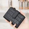 A hand holds a black PU leather bifold wallet with a gold zipper and ID window.