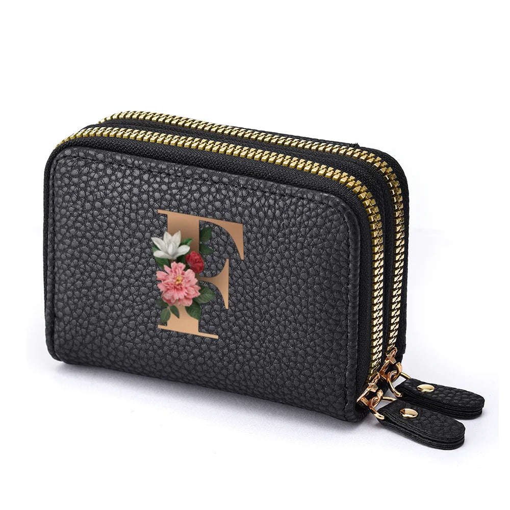 Black faux leather mini wallet with a gold zipper and a floral letter print