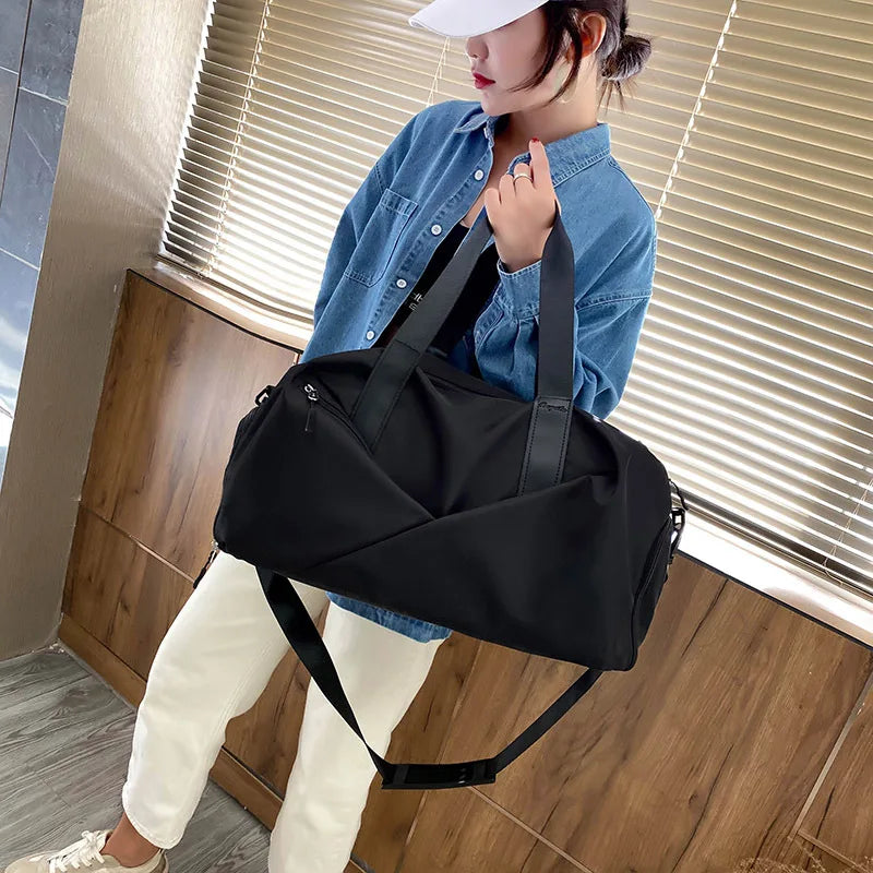 A woman is holding a black nylon gym and travel duffel bag with a shoulder strap in front of her.