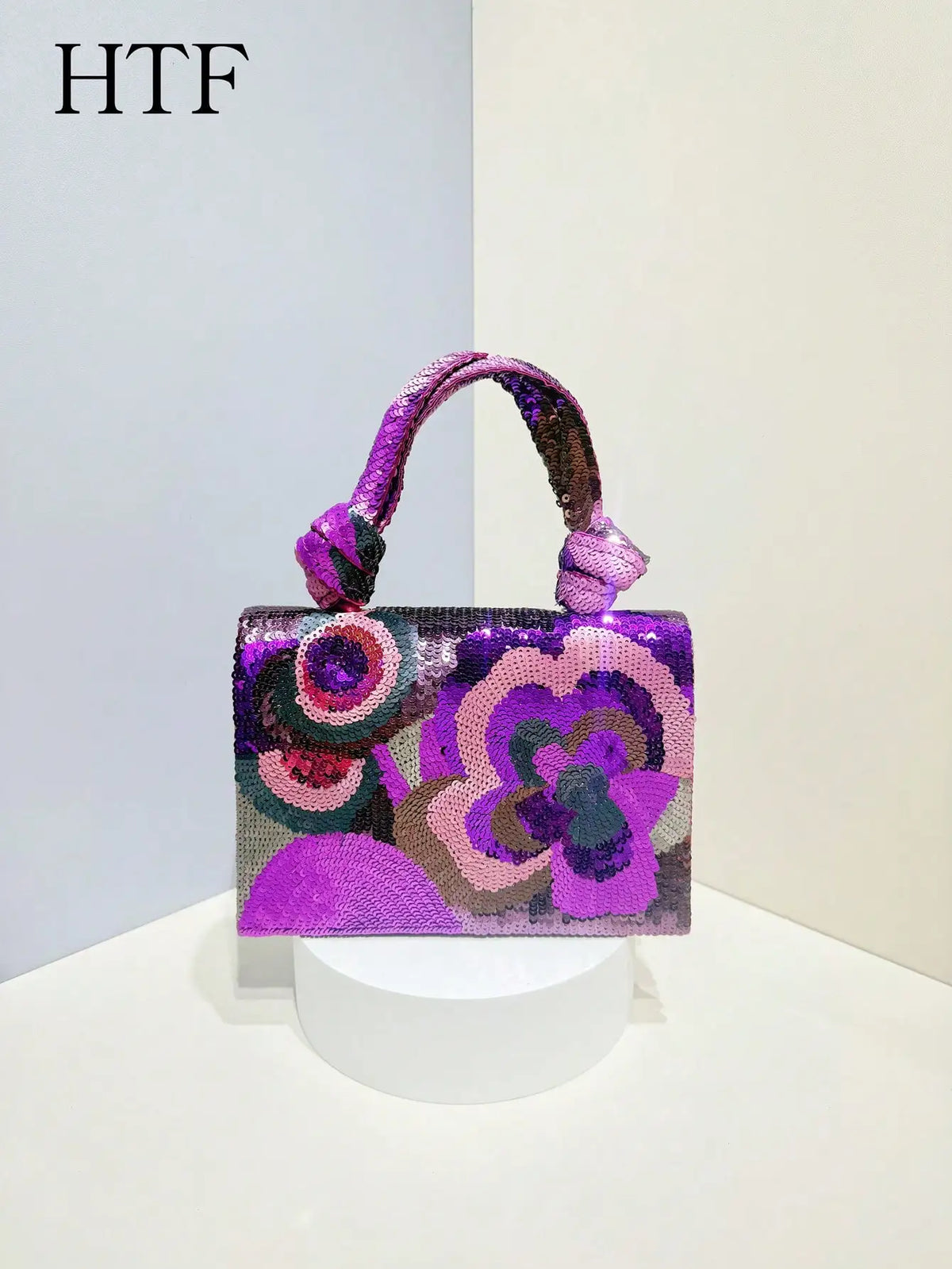 A purple and pink sequin embroidered floral clutch bag with a purple strap displayed on a white pedestal.