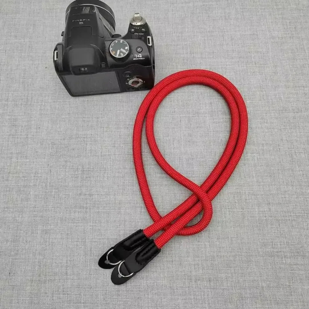 A black camera body and a red adjustable shoulder strap are displayed on a gray fabric background.