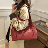 A woman holds a red leather everyday large-capacity shoulder tote bag against a light colored dress.