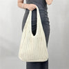 A woman holds a cream-colored bohemian knit shoulder bag against a gray background.