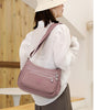 A woman wearing a white shirt and hat carries a mauve nylon crossbody shoulder bag.