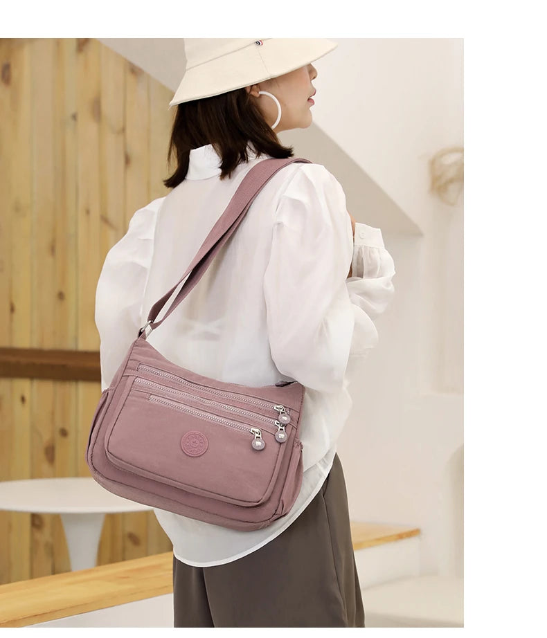 A woman wearing a white shirt and hat carries a mauve nylon crossbody shoulder bag.
