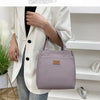 A woman holds a mauve insulated lunch bag in a white blazer, set against a bright indoor background.
