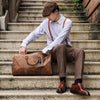 Ein junger Mann sitzt auf Steinstufen und hält eine vintage geprägte Leder-Tasche.