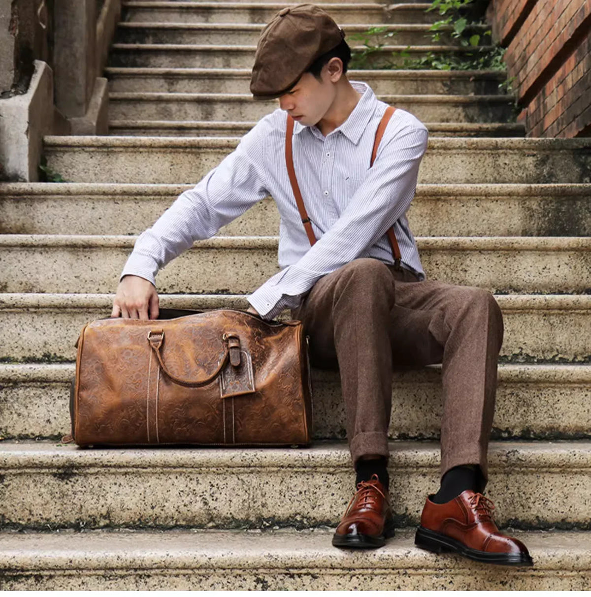 Ein junger Mann sitzt auf Steinstufen und hält eine vintage geprägte Leder-Tasche.