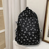 Mochila negra con estampado floral y múltiples bolsillos colgando contra una pared blanca.