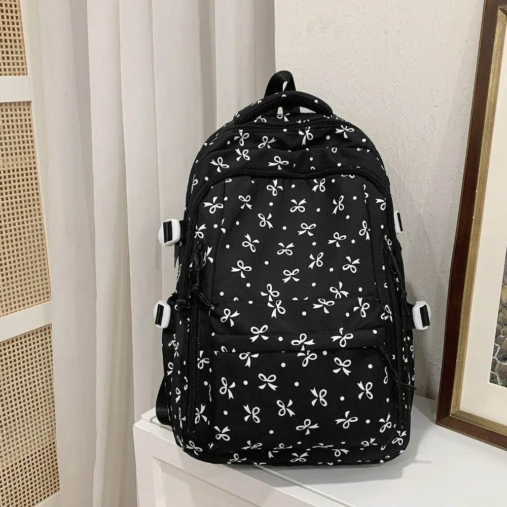 Mochila negra con estampado floral y múltiples bolsillos colgando contra una pared blanca.