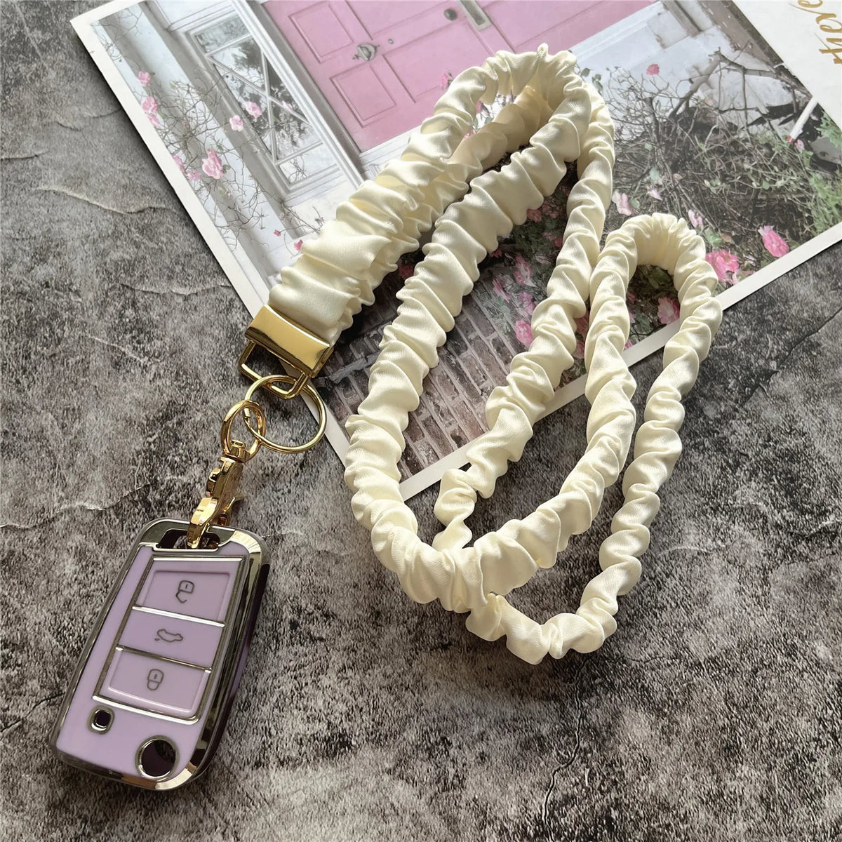 Cremfarbiger Stoff-Lanyard mit goldenem Schlüssel, präsentiert auf einer strukturierten grauen Oberfläche.