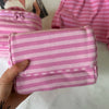 A hand holds a pink striped makeup bag with a flip-top mirror, next to pink striped shorts.