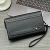 A black crocodile pattern clutch bag resting on a wooden desk next to a silver laptop and a white cup.