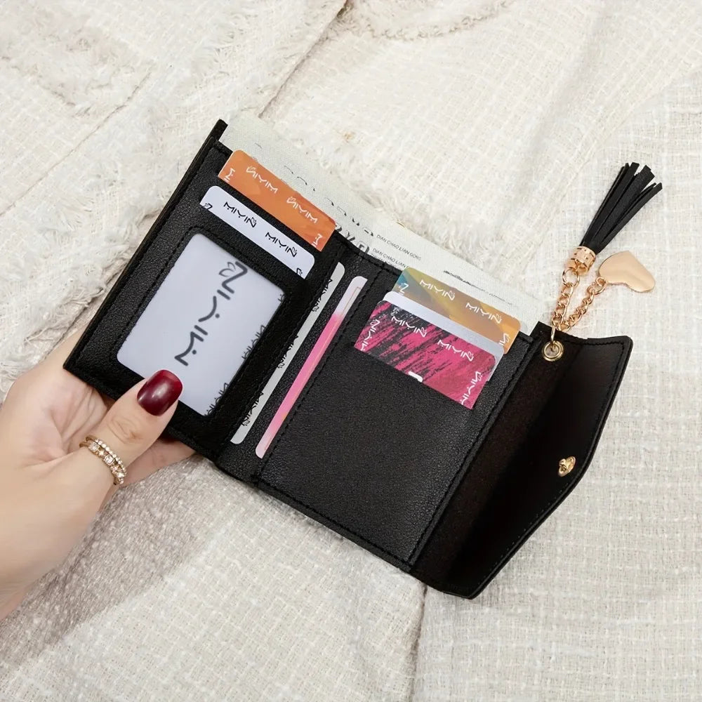A black PU leather coin clutch wallet with various cards and a gold tassel is held in a hand on a light fabric background.