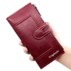 A hand holds a maroon leather wallet with a zipper closure and a flap design.