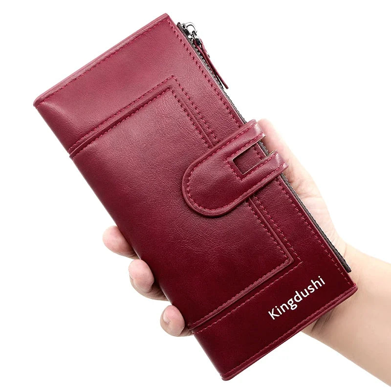 A hand holds a maroon leather wallet with a zipper closure and a flap design.
