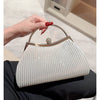 A hand holds a light silver pleated glitter evening handbag with a top handle and chain strap against a white background.
