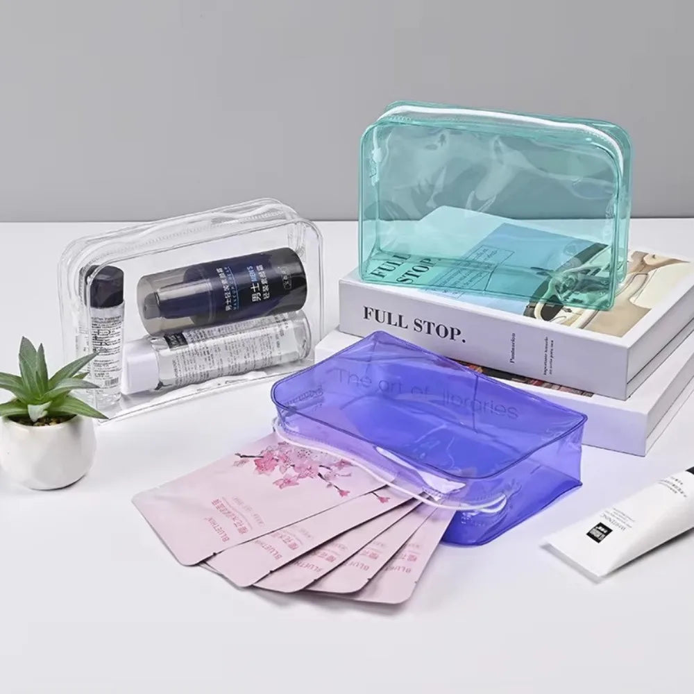 A collection of clear and purple PVC travel makeup bags and a skincare product are displayed on a white surface.