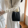 A woman wearing a white dress holds a black PU leather pleated crossbody bag.