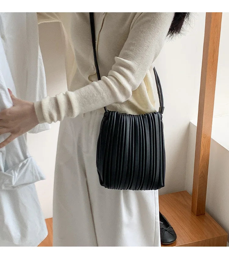 A woman wearing a white dress holds a black PU leather pleated crossbody bag.