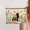 Una mano sostiene una bolsa de cosméticos beige con estampado floral de gatos negros y diversas flores silvestres coloridas.