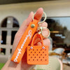 An orange silicone heart beach bag keychain is held in a hand against a blurred outdoor background.