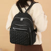 A black waterproof women's travel backpack worn by a person in a cream sweater.