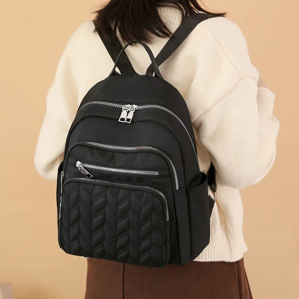 A black waterproof women's travel backpack worn by a person in a cream sweater.