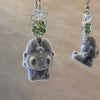 A soft gray plush toy of Toothless the dragon is attached to a silver keychain with green beads.