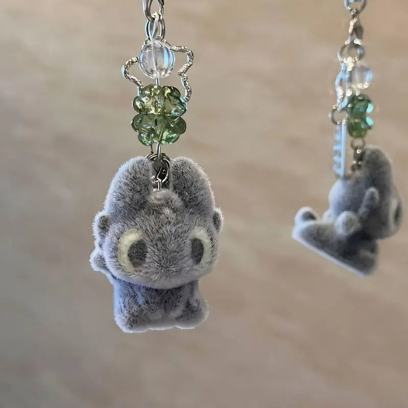 A soft gray plush toy of Toothless the dragon is attached to a silver keychain with green beads.