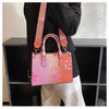 A pink and orange ladies' shoulder tote bag is carried by a person in a black top, resting on a dark shelf.
