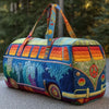 A colorful quilted travel duffle bag with patterned fabric and striped handles resting on a gray surface.
