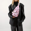 A woman wearing a black leather jacket and pants holds a pink quilted crossbody sling bag with a floral pattern.