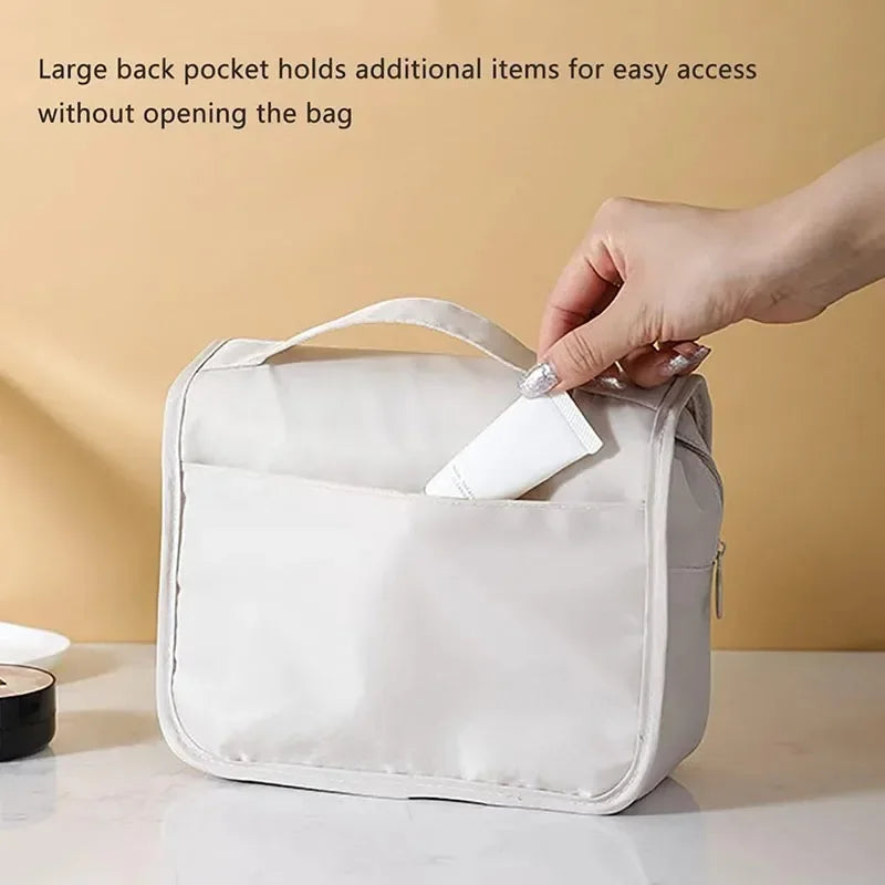 A hand is accessing a large back pocket on a white waterproof makeup organizer bag to retrieve an item.