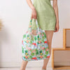 A person holds a large, reusable shopping bag with a floral pattern in a light green dress.