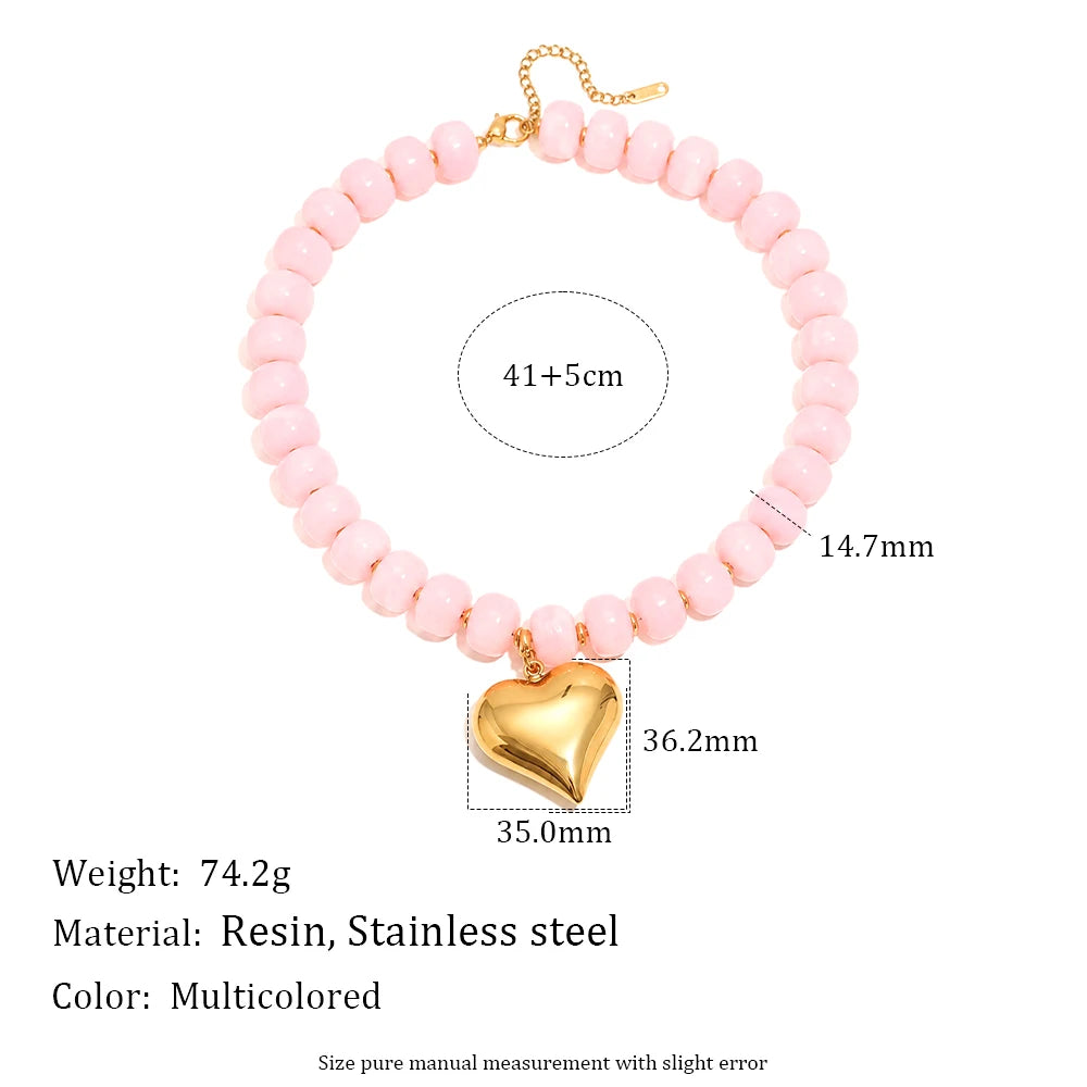 A pink bead necklace featuring a gold chain and a heart-shaped gold charm, made with resin and stainless steel.
