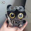 Colgante llavero de peluche de gato negro con ojos grandes y accesorio de guitarra, sostenido por una mano.