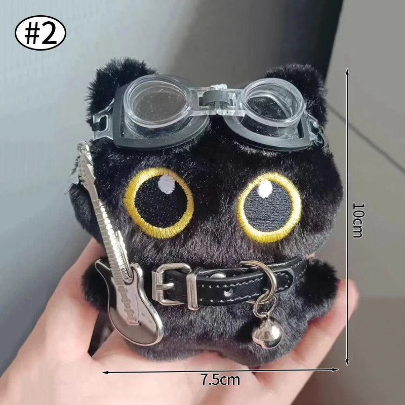 Colgante llavero de peluche de gato negro con ojos grandes y accesorio de guitarra, sostenido por una mano.