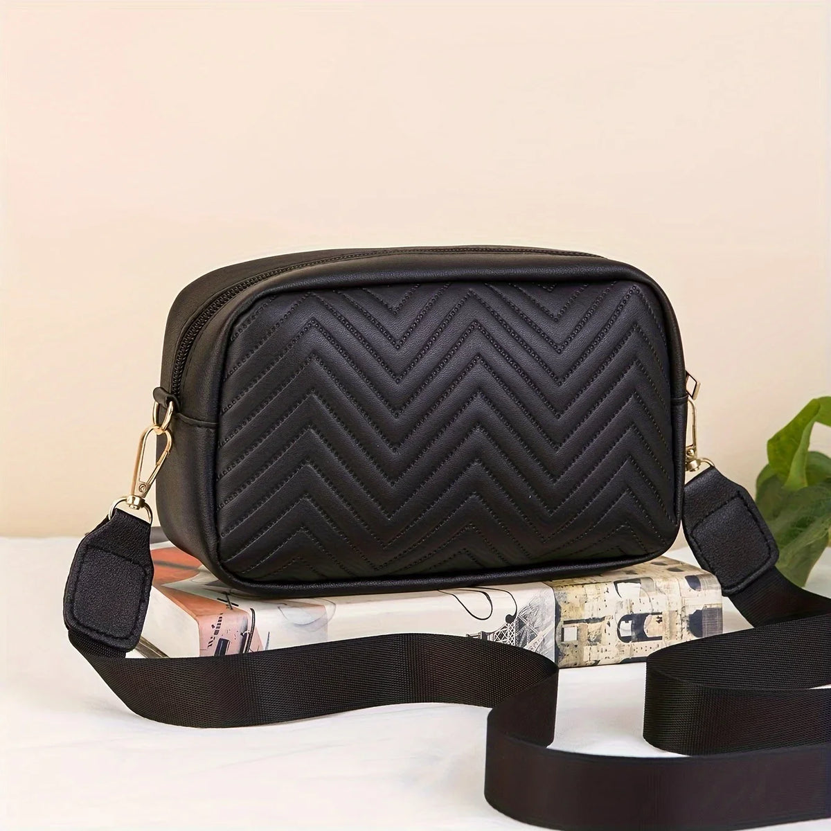 Schwarze gesteppte minimalistische Crossbody-Tasche mit schwarzem Riemen auf weißem Untergrund.