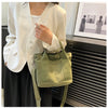 A woman models a light green canvas crossbody bag with an adjustable strap and multiple pockets against a dark background.
